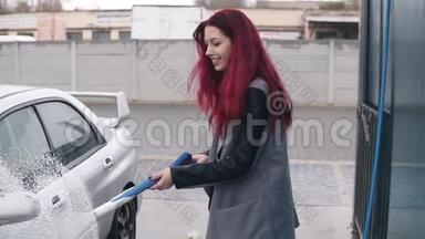 一位红头发的年轻女士在她的银色跑<strong>车上</strong>涂上泡沫，并在自助洗<strong>车上</strong>涂上特殊的喷气式飞机